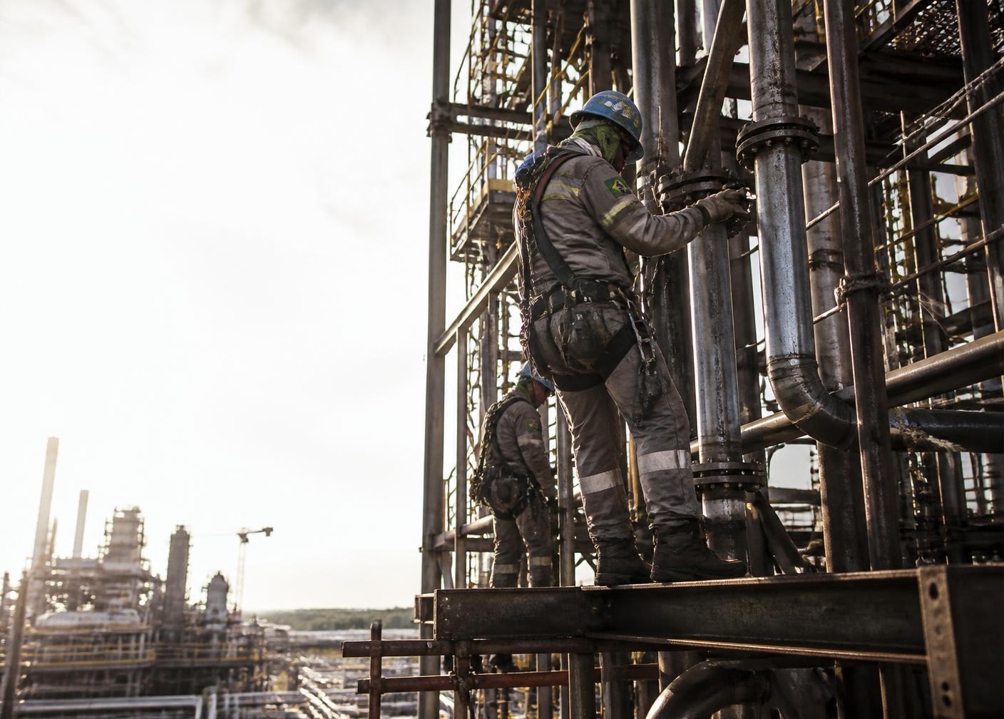 Profissionais com capacete e cinto de segurança em montagem industrial de estruturas metálicas